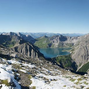 Jezero Lünersee z vrcholu Saulakopf (2517 m). Vlevo Schafgafall (2414 m), vpravo Seekopf (2698 m). Za jezerem Kanzelköpfe (2437 m) a Girenspitze (2394 m) ve Švýcarsku. pohoří Rätikon, Alpy.