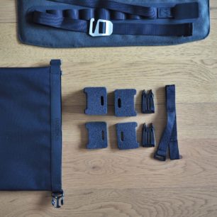 Vybalené distanční podložky, plastové spony a popruh se suchým zipem pro uchycení k hlavové trubce. Vlevo strana drybagu s reflexním prvkem Scape Handlebar Rollu.
