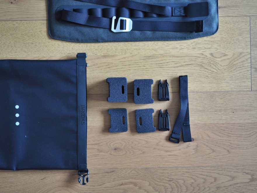 Vybalené distanční podložky, plastové spony a popruh se suchým zipem pro uchycení k hlavové trubce. Vlevo strana drybagu s reflexním prvkem Scape Handlebar Rollu.