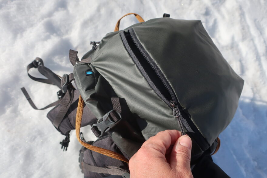 Vrchní kapsa Thule Stir Alpine je dobře přístupná pro věci rychlé potřeby. Je nepromokavá. Oranžová poutka dobře dlouhá k snadné manipulaci s batohem.