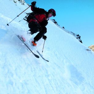 Přeskakovaný oblouk na velmi strmém svahu focený z nejmenší možné vdálenosti, rušivě působí na pozadí sluncem zalité svahy.