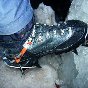 Lezecká mačka s kovovými třmeny, upnutá na kožené botě se žlábky.