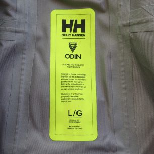 Vnitřní etiketa bundy HELLY HANSEN Odin 9 Worlds Jkt kromě názvu, velikosti obsahuje i příběh.
