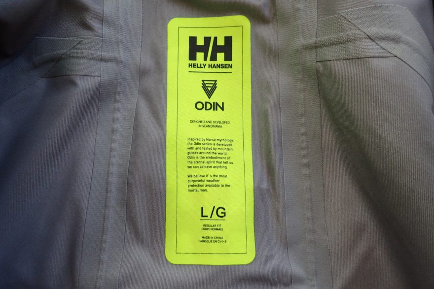Vnitřní etiketa bundy HELLY HANSEN Odin 9 Worlds Jkt kromě názvu, velikosti obsahuje i příběh.