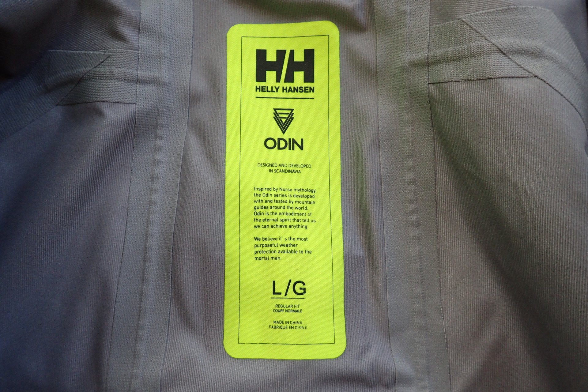 Vnitřní etiketa bundy HELLY HANSEN Odin 9 Worlds Jkt kromě názvu, velikosti obsahuje i příběh.
