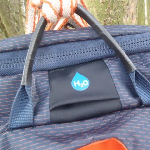 Průchodka pro hadičku vodního vaku nebo na protažení popruhu pro fixaci lana na batoh OSPREY Mutant 22.