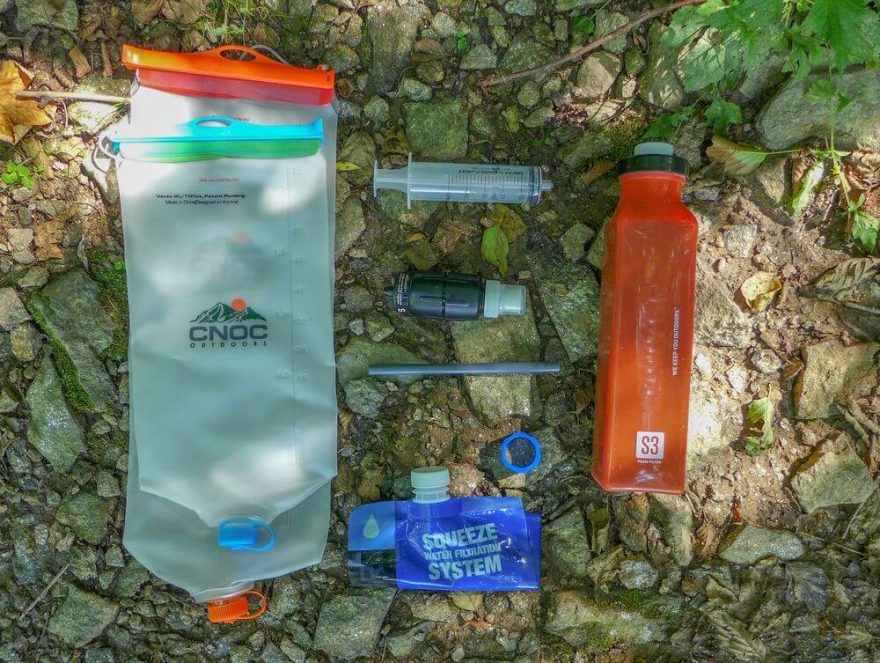 Kompletní filtrační set. Zprava a shora: lahev S3, stříkačka na průplach, filtr Sawyer Micro Squeeze, brčko, redukce pro PET lahve, skládací lahev Sawyer, skládací lahve CNOC.